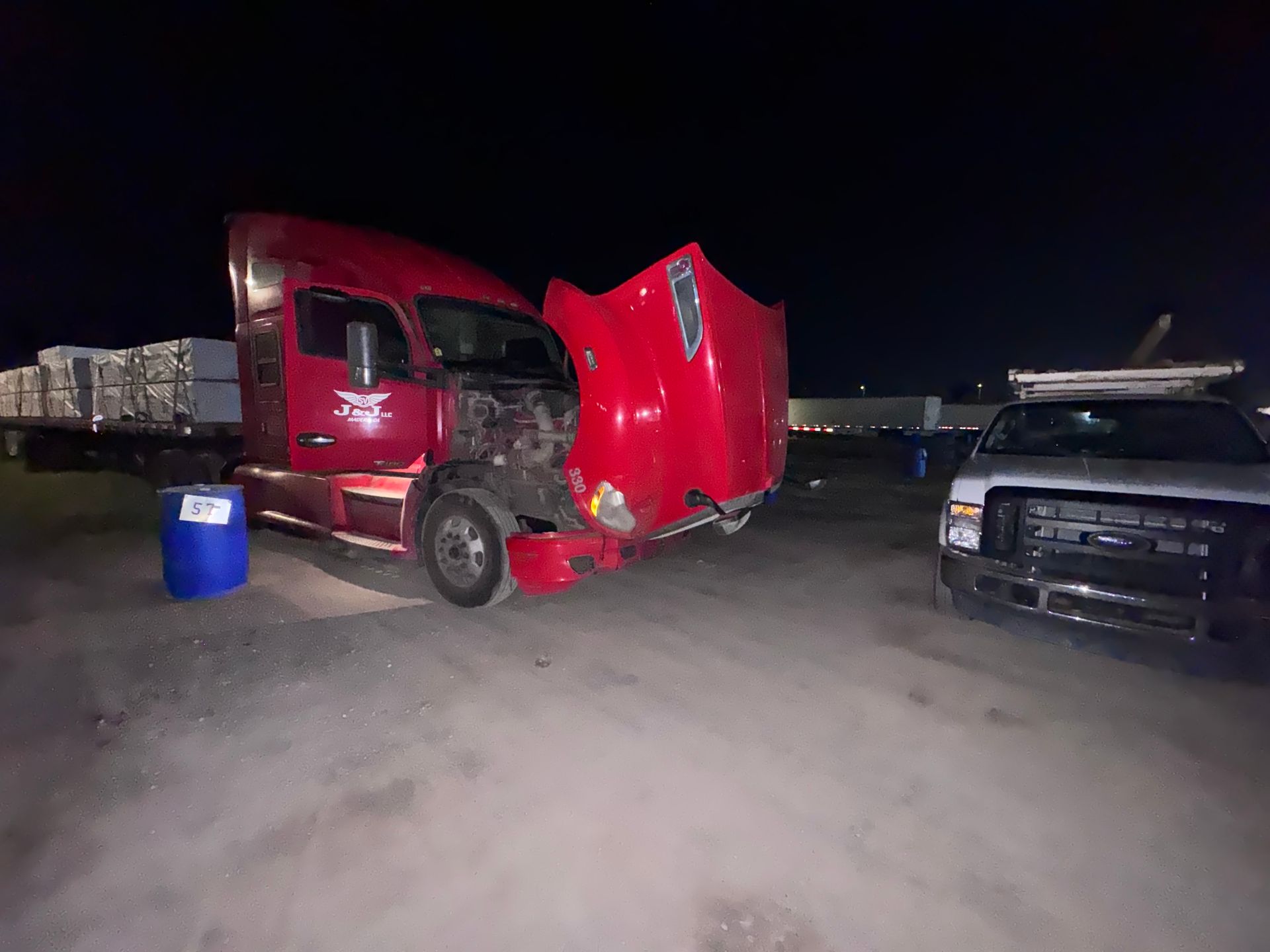 Red semi-truck with front-end damage; parked next to a white truck at night.