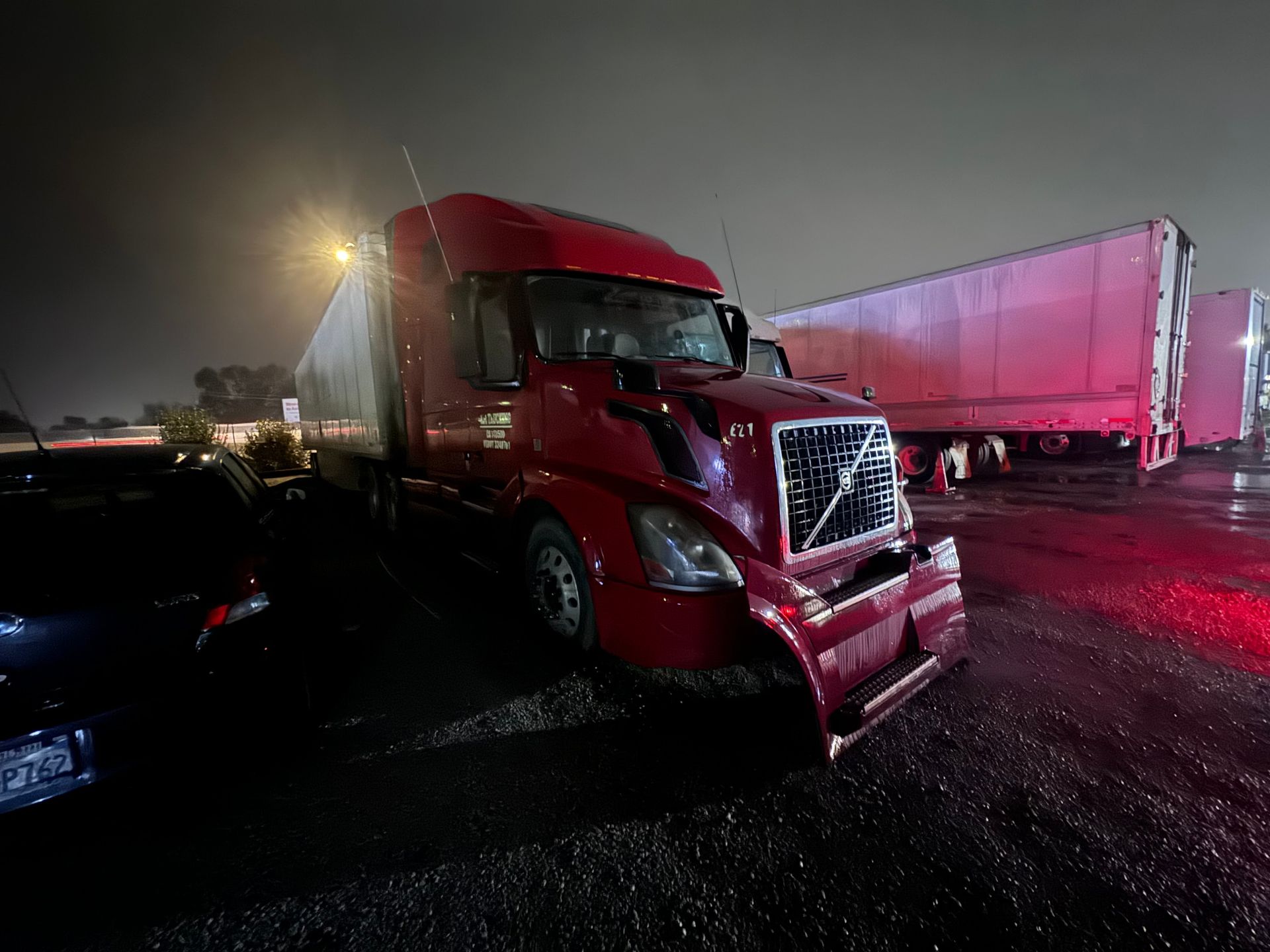 Red semi-truck with front-end damage parked at night, other trailers in the background.