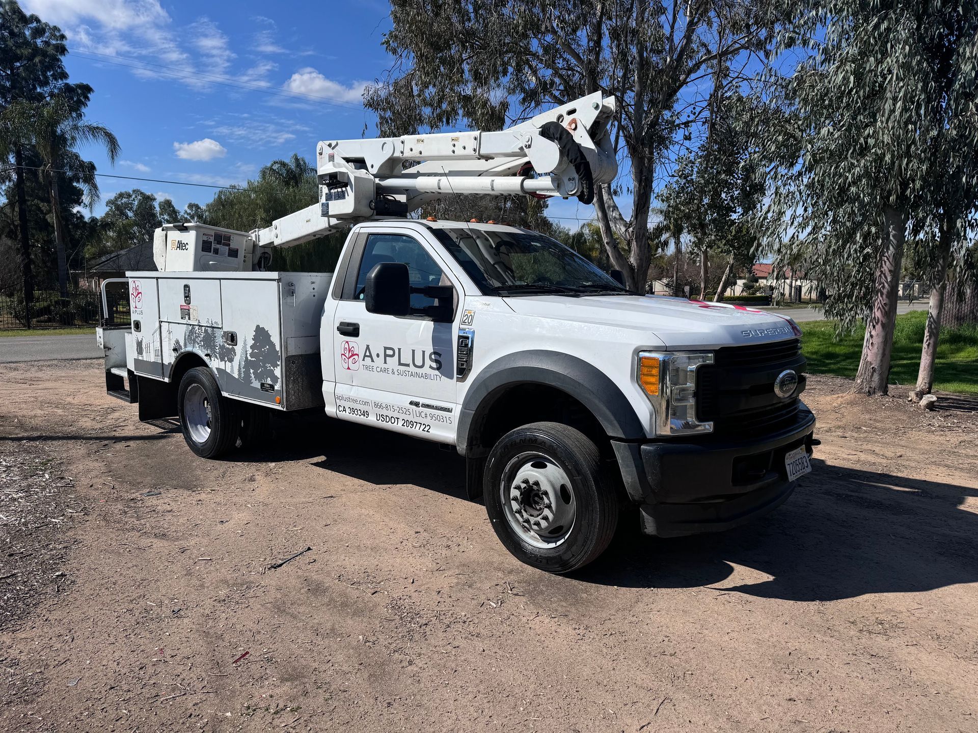 White utility truck with an extended arm, parked on dirt.