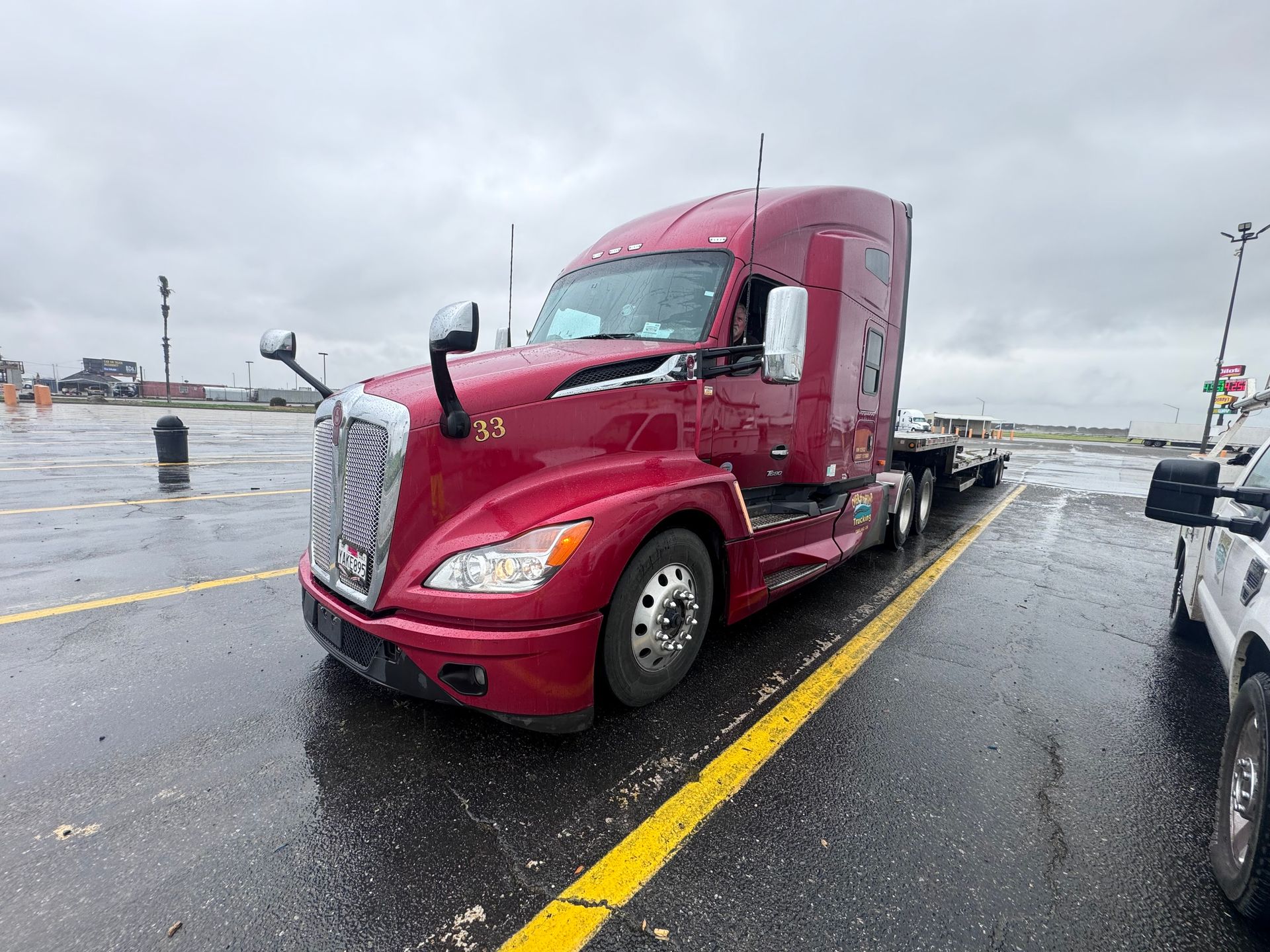 Red semi-truck parked on wet asphalt, gray overcast sky, yellow lines.