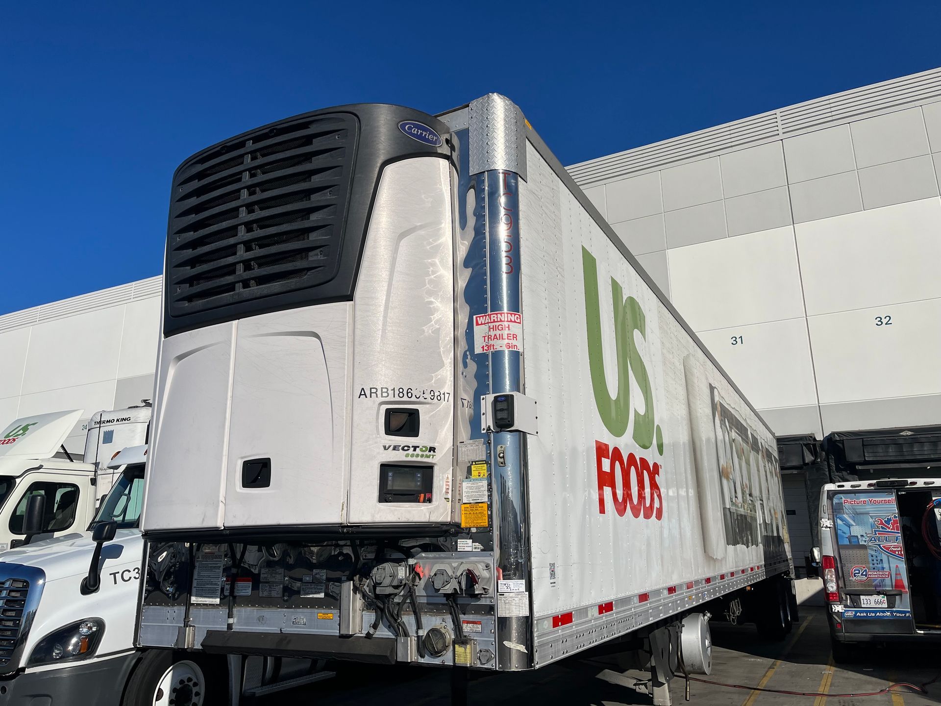Refrigerated US Foods trailer parked near a loading dock under a blue sky.
