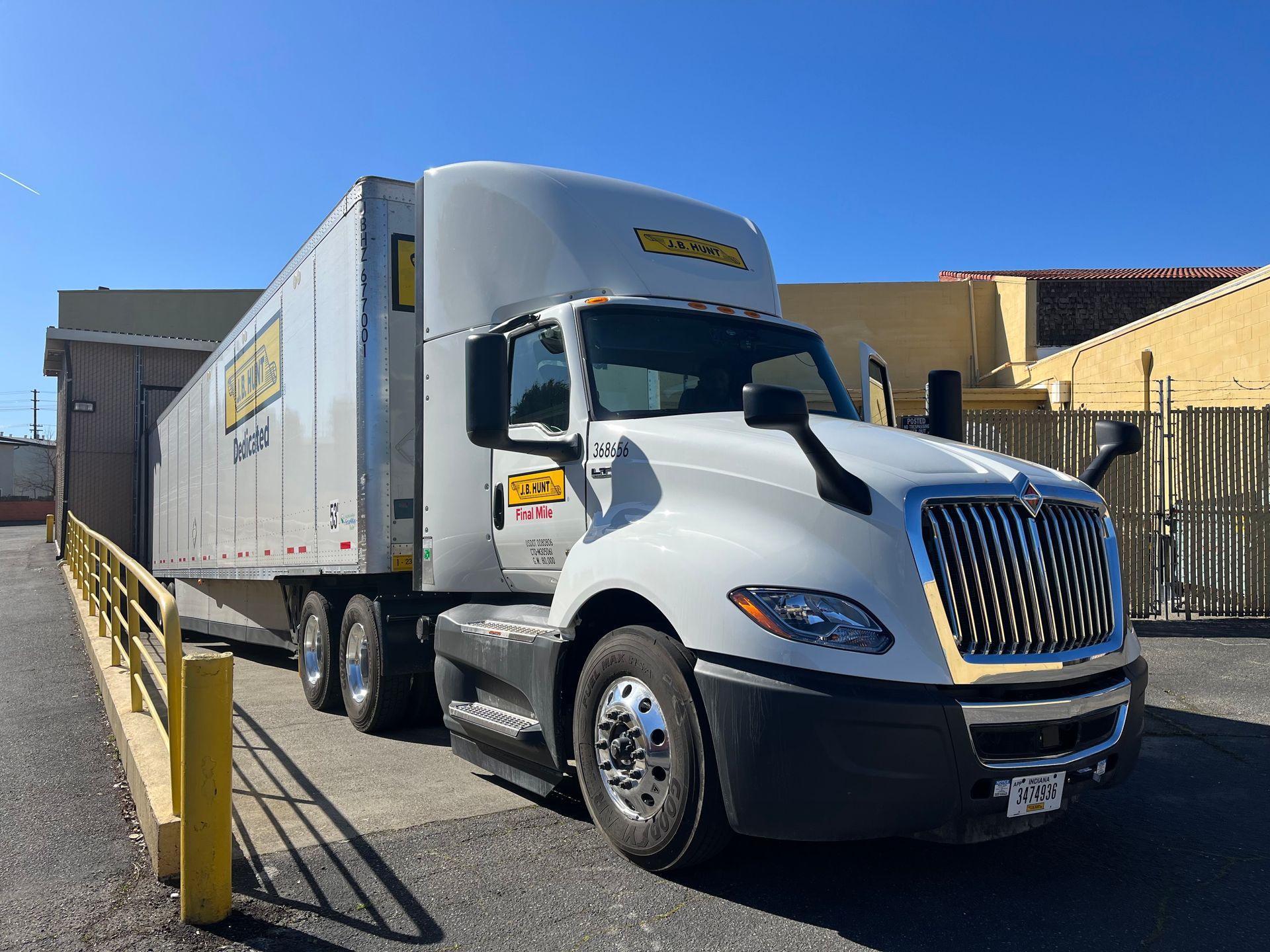 White semi-truck with trailer parked at a loading dock under a clear blue sky.