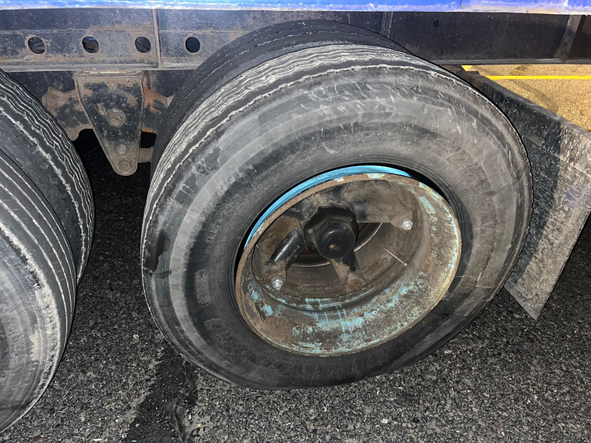 Close-up of a flat truck tire. The wheel is rusted, and the tire is deflated.