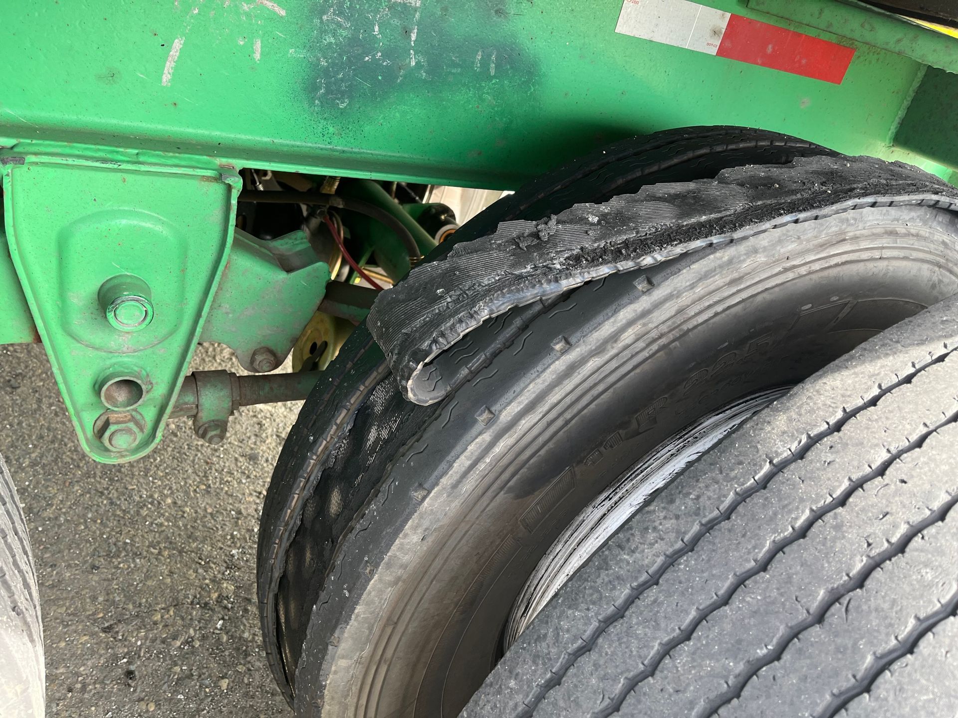 Damaged truck tire with shredded sidewall on a green trailer, showing wear and tear.