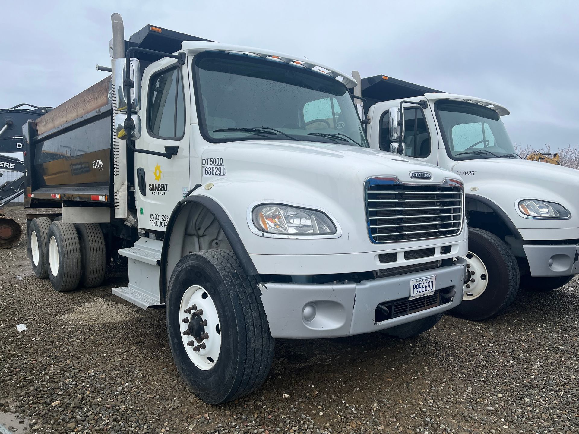 Two white dump trucks parked on gravel, one with its bed raised, in an outdoor setting.