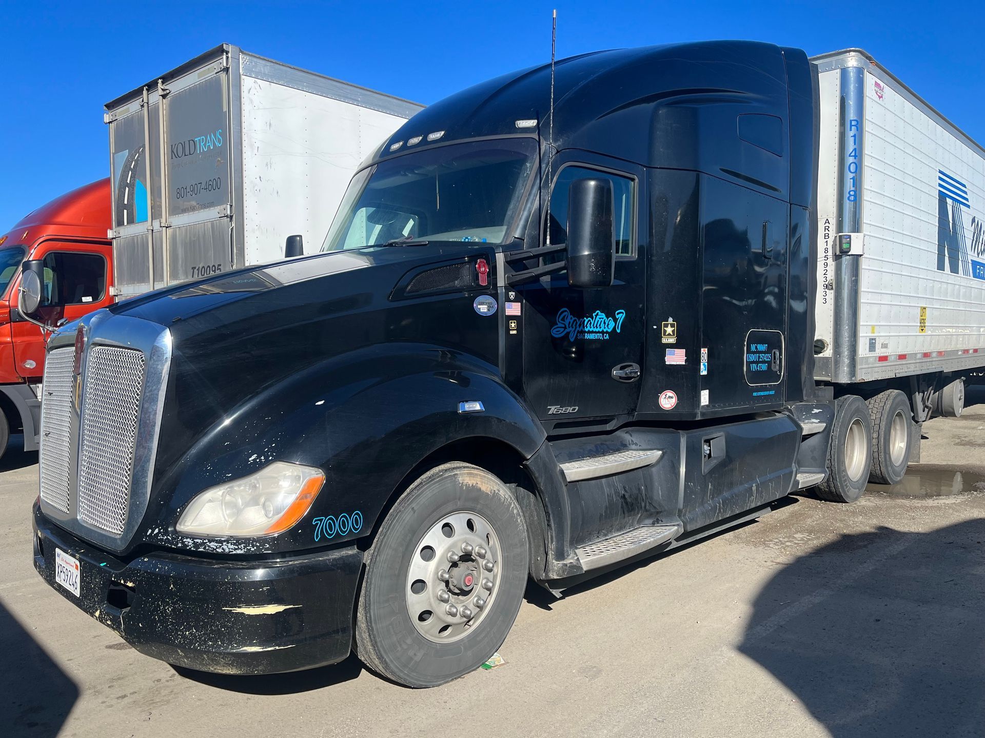 Black semi-truck parked outdoors. It has a white trailer and logos on the side, under a clear sky.