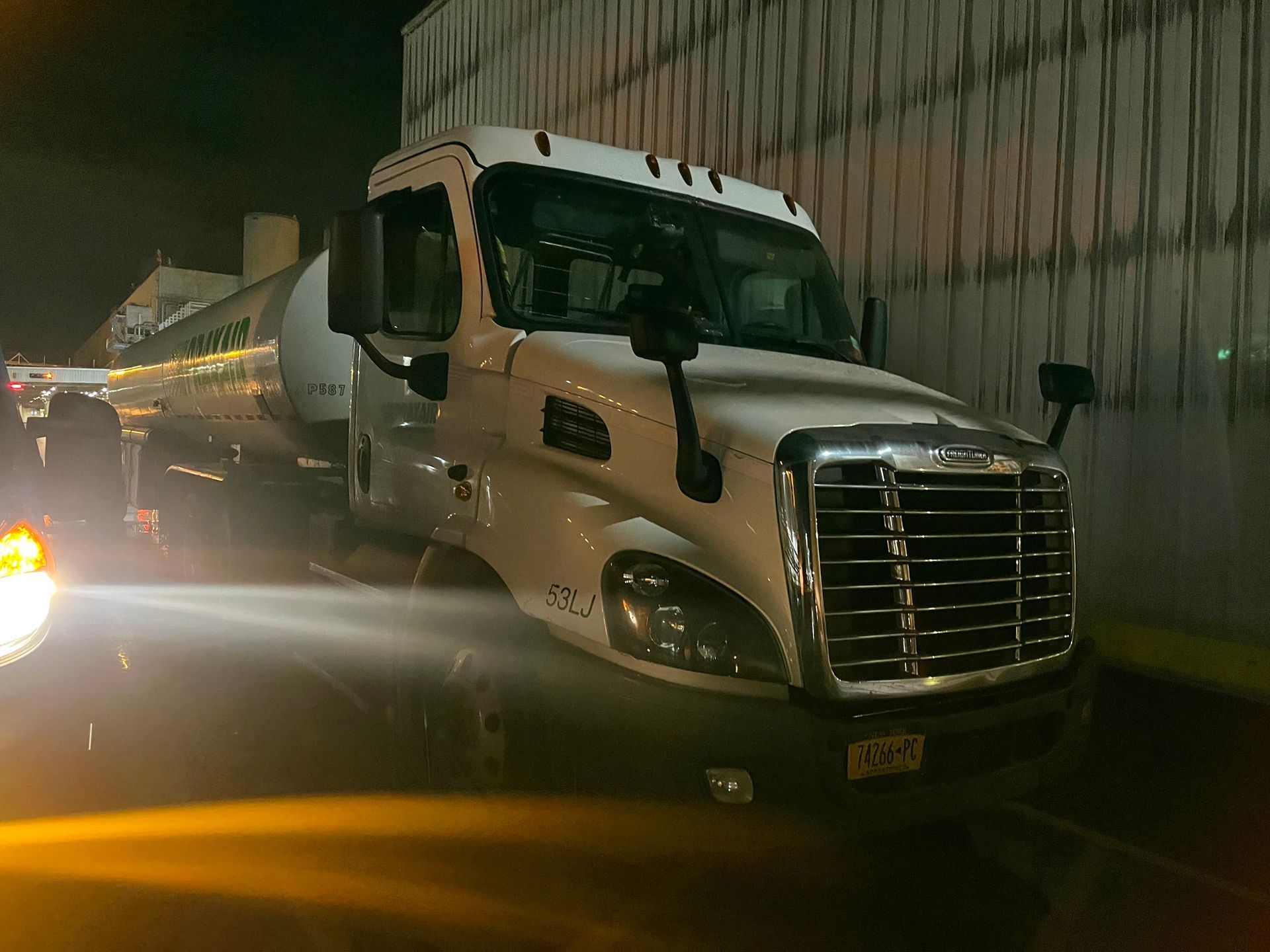 White tanker truck parked at night, next to a building.