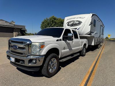 White Ford truck towing a large white fifth-wheel trailer on a sunny road.