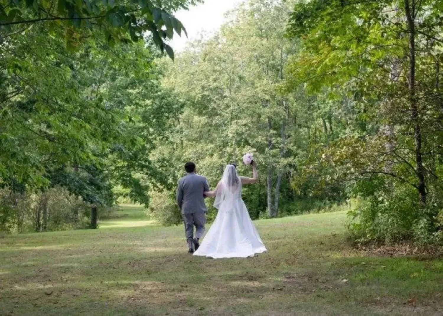 A bride and groom are walking down a path in the woods.