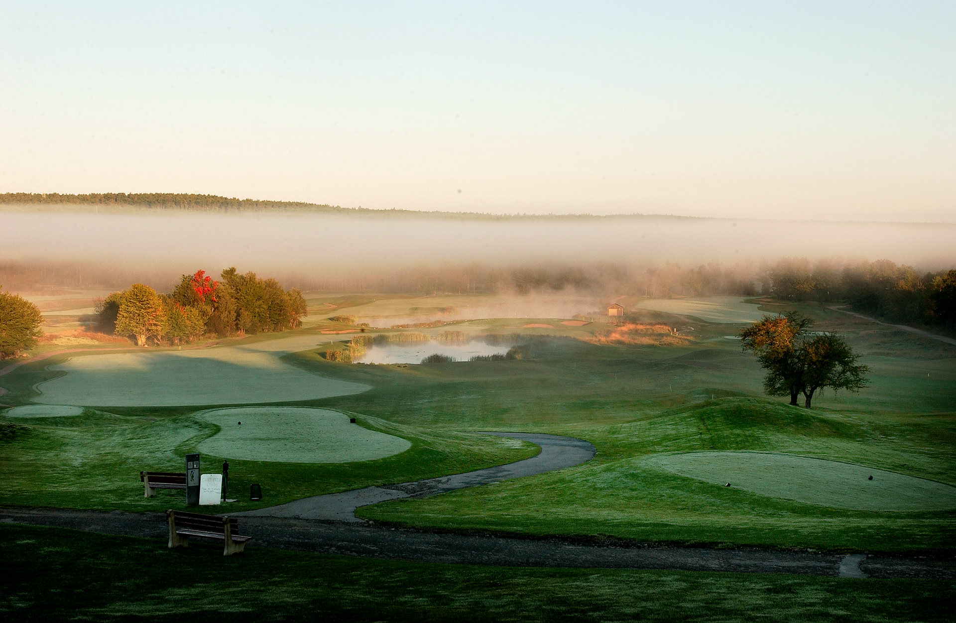 A foggy golf course with a red flag on the green.