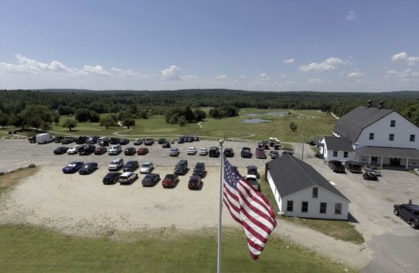 An american flag is flying in front of a parking lot filled with cars.