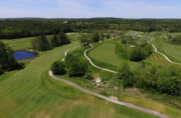 An aerial view of a golf course surrounded by trees and a road.