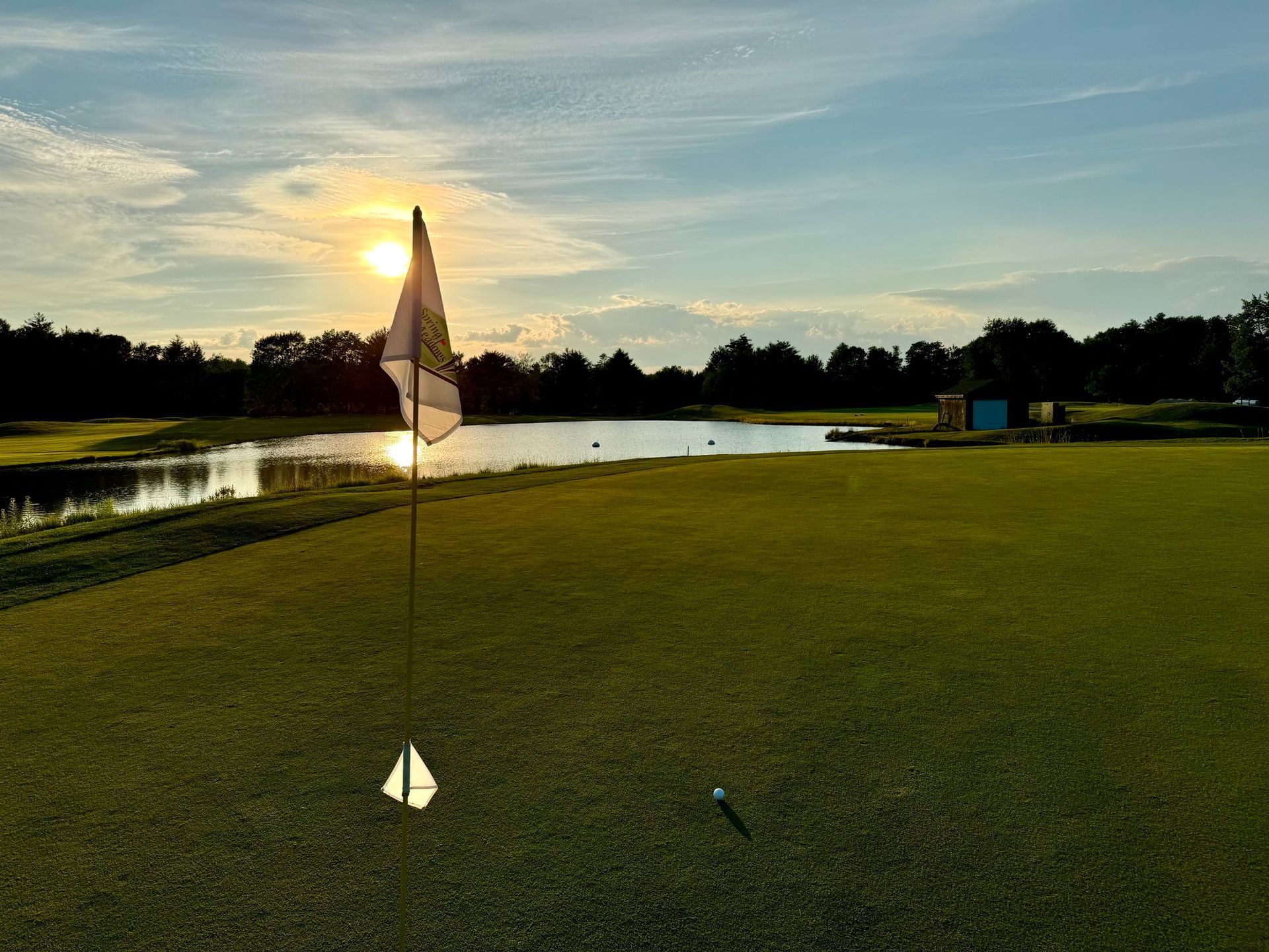 A golf course with a flag on the green and a lake in the background.