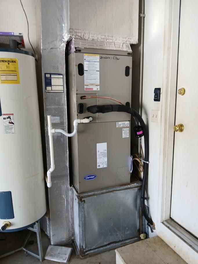 HVAC system and hot water heater beside a door. Gray metal units with ductwork and pipes in a corner.