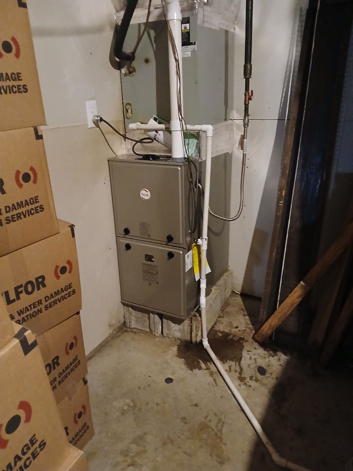 Furnace unit in a basement with white PVC pipe and cardboard boxes stacked on the left.
