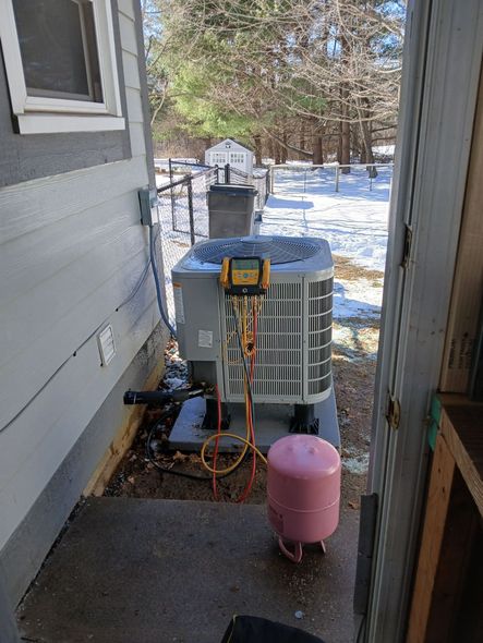 HVAC unit being serviced outside a building in a snowy environment. Pink tank, gauges, and hoses connected.