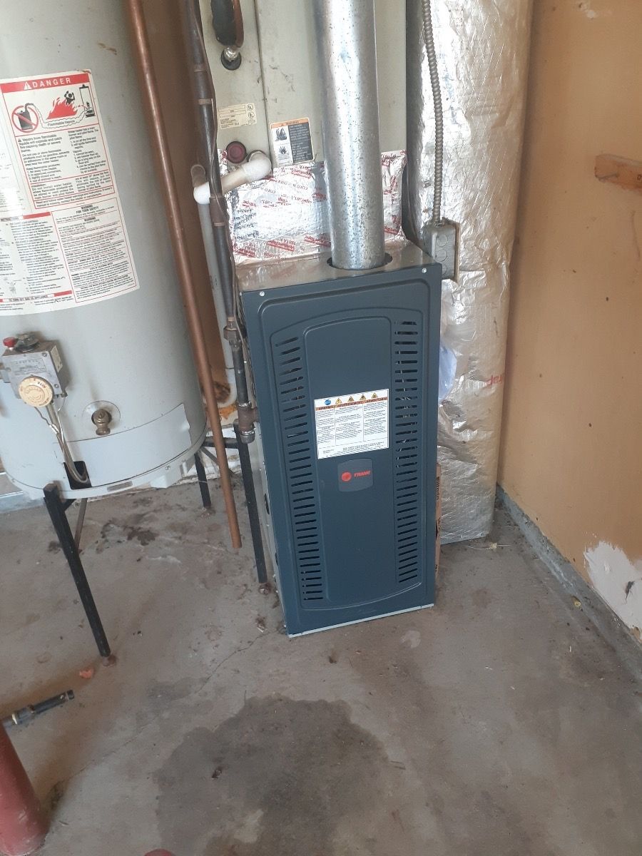 Furnace and water heater in a basement. The furnace is gray with a vent above. A water heater is to the left.
