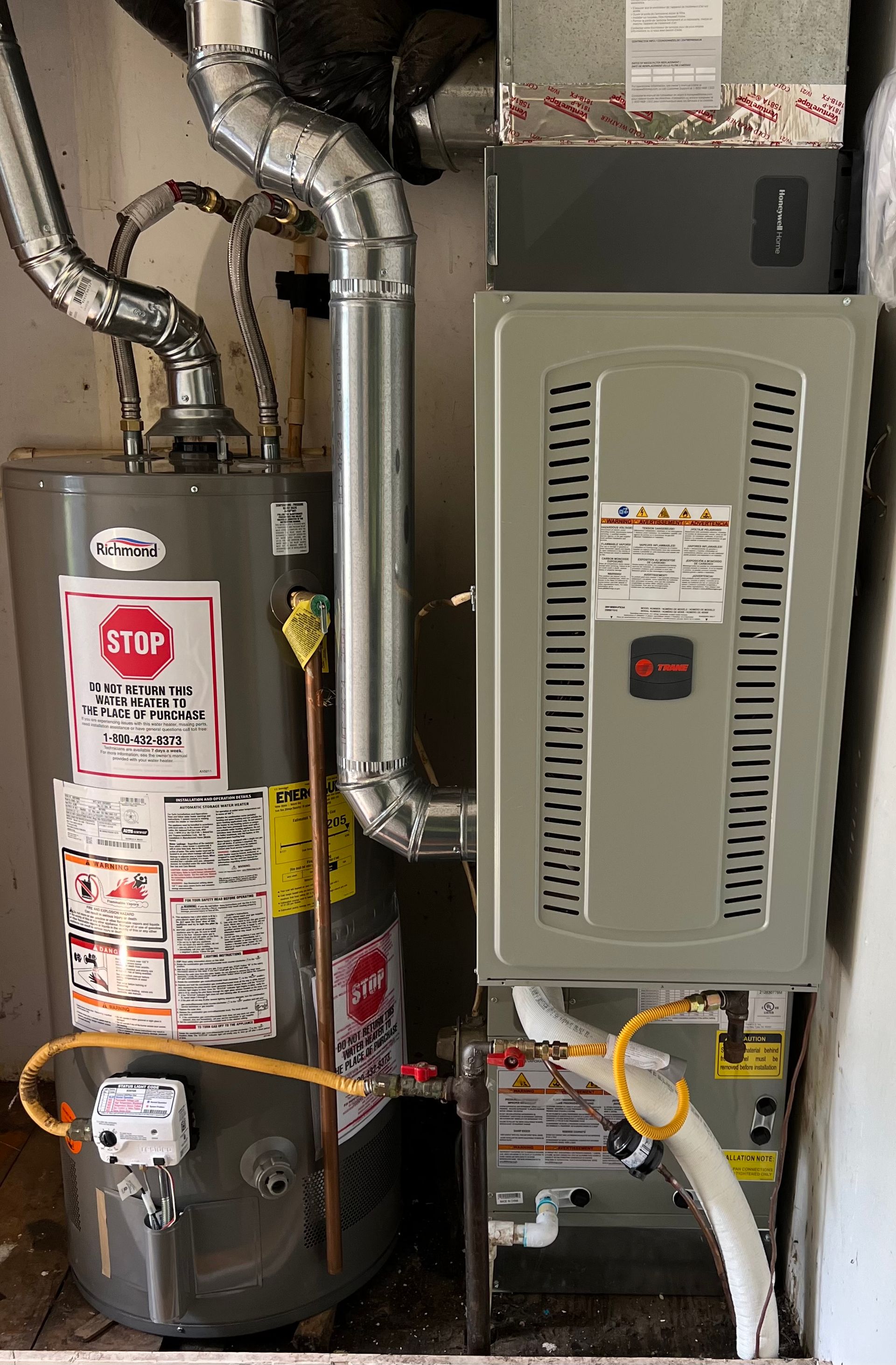 Water heater and furnace in a utility closet with pipes, ductwork, and safety labels.