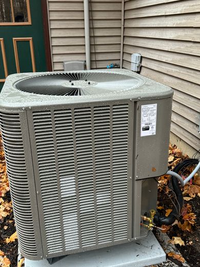 Gray air conditioning unit next to a building with fall leaves around the base.