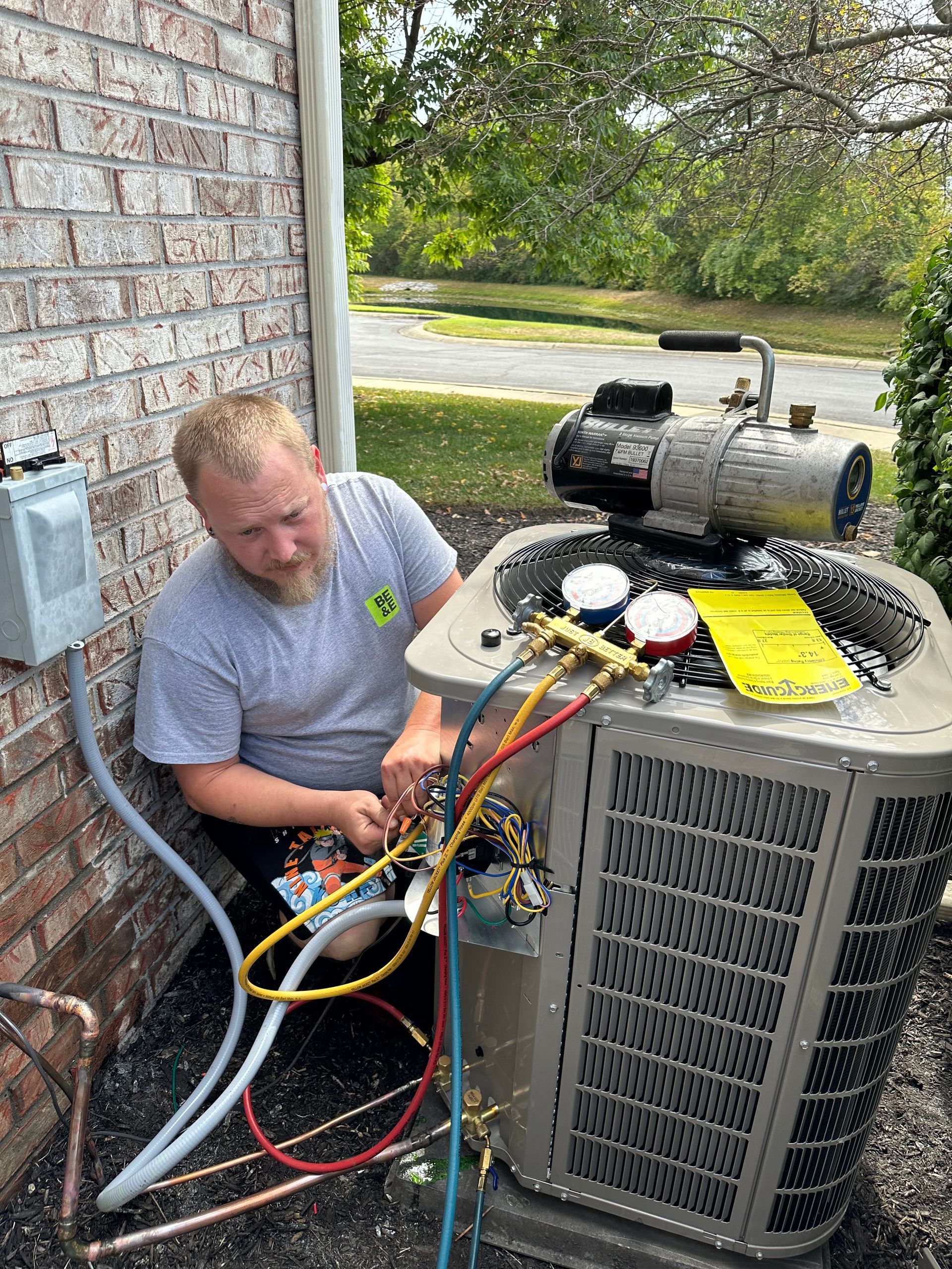 HVAC technician working on an air conditioning unit outdoors near a brick wall, connecting gauges, focusing intently.