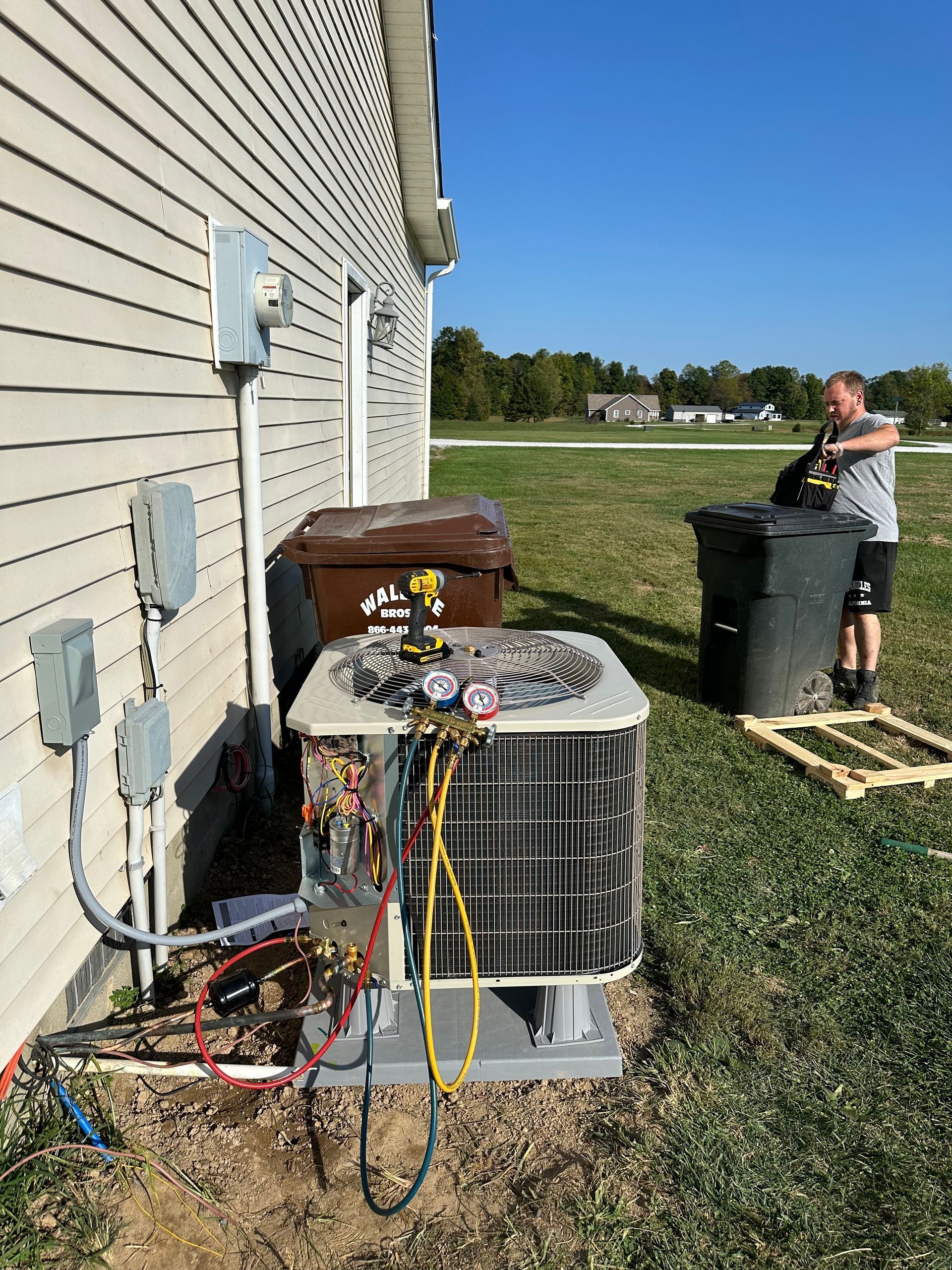 HVAC technician working on an air conditioner unit outside a house.  Blue sky, green grass.