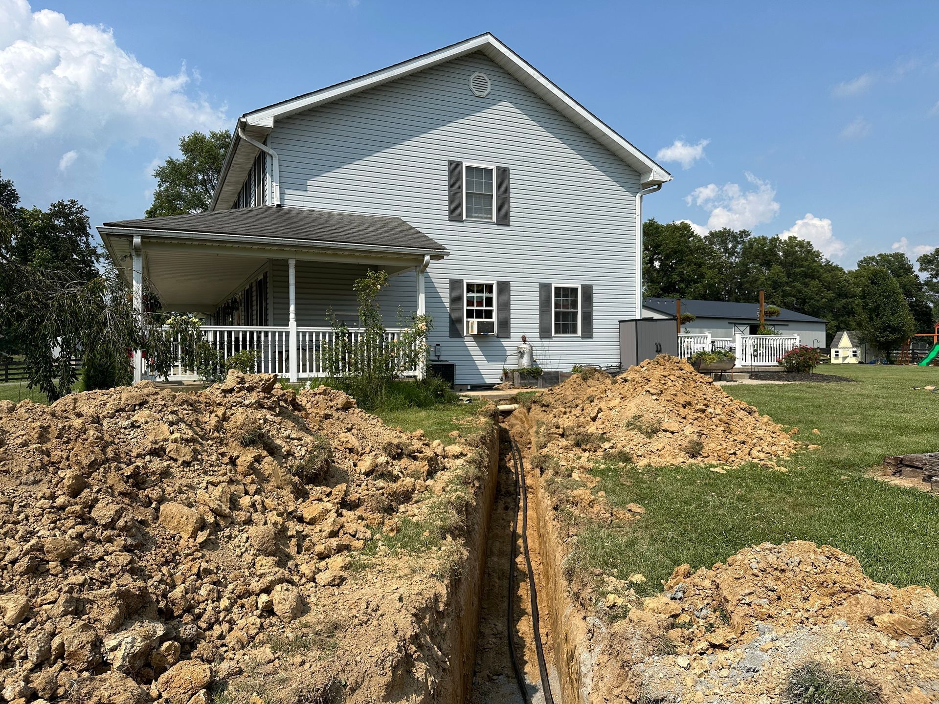 A trench dug in front of a two-story house, with piles of dirt on either side.