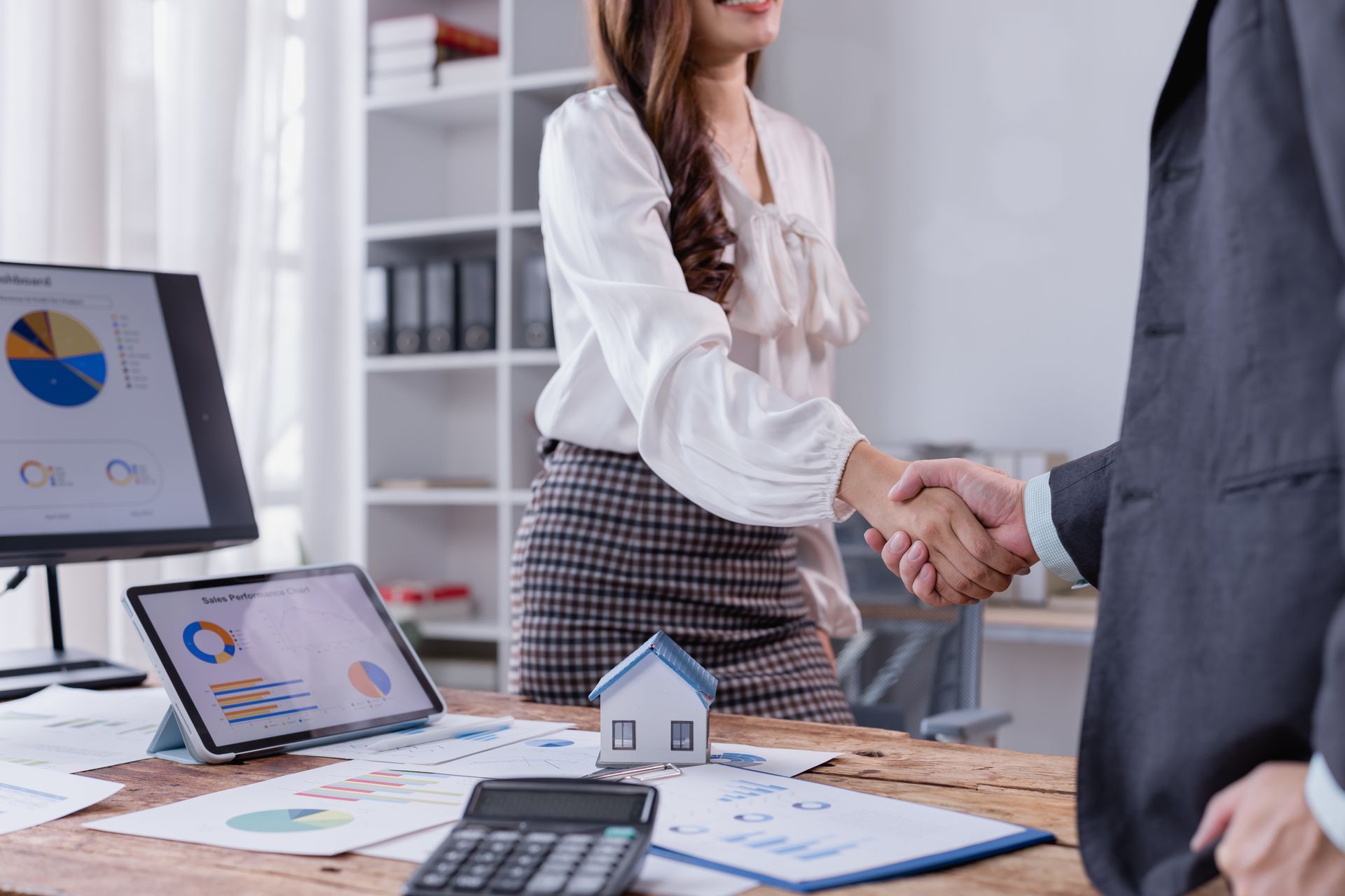 Business professionals shaking hands over a desk house model, symbolizing a real estate agreement.