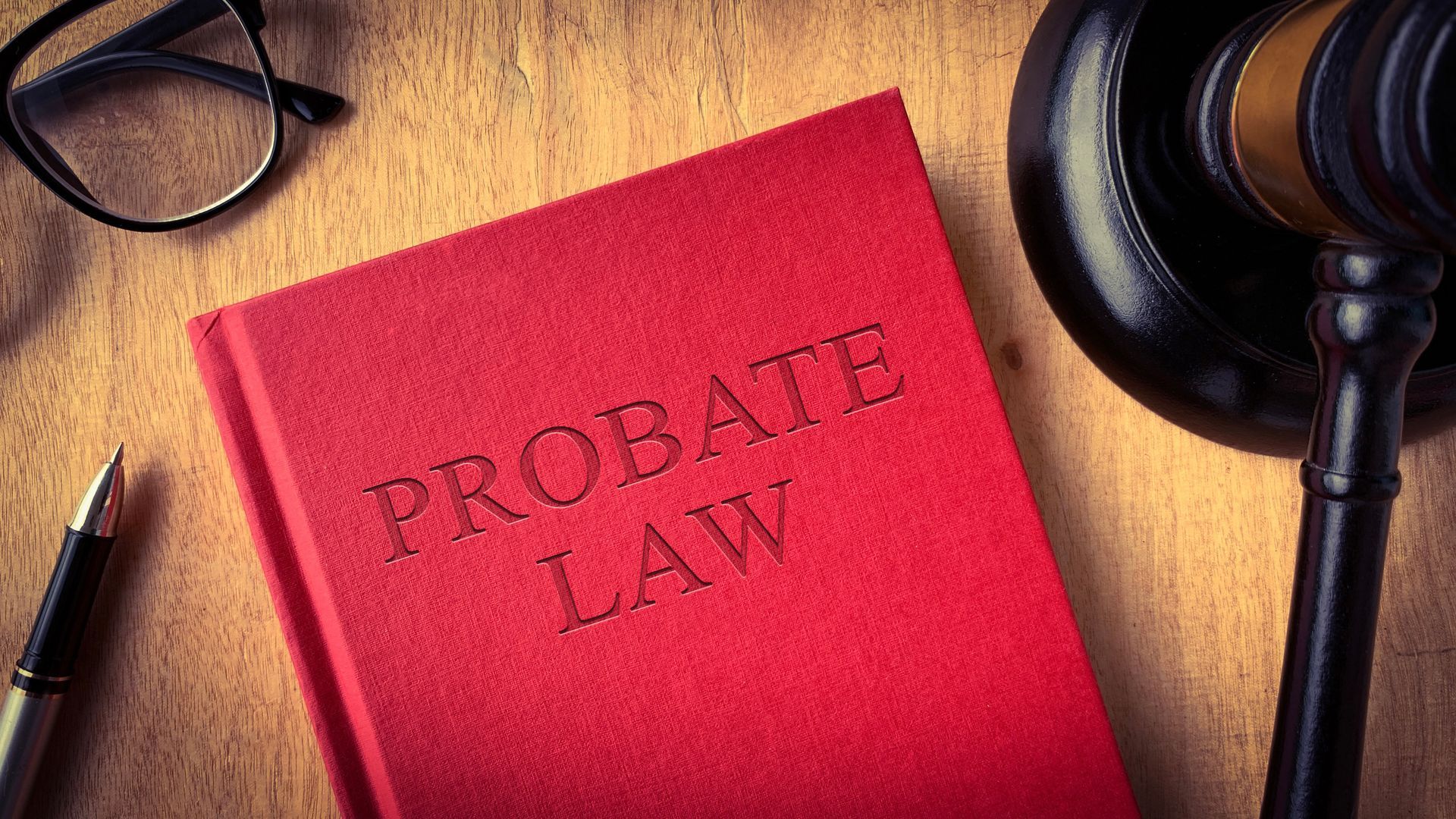Probate law book with gavel, glasses, and pen on wooden table. Probate law book with gavel, glasses, and pen on wooden table.