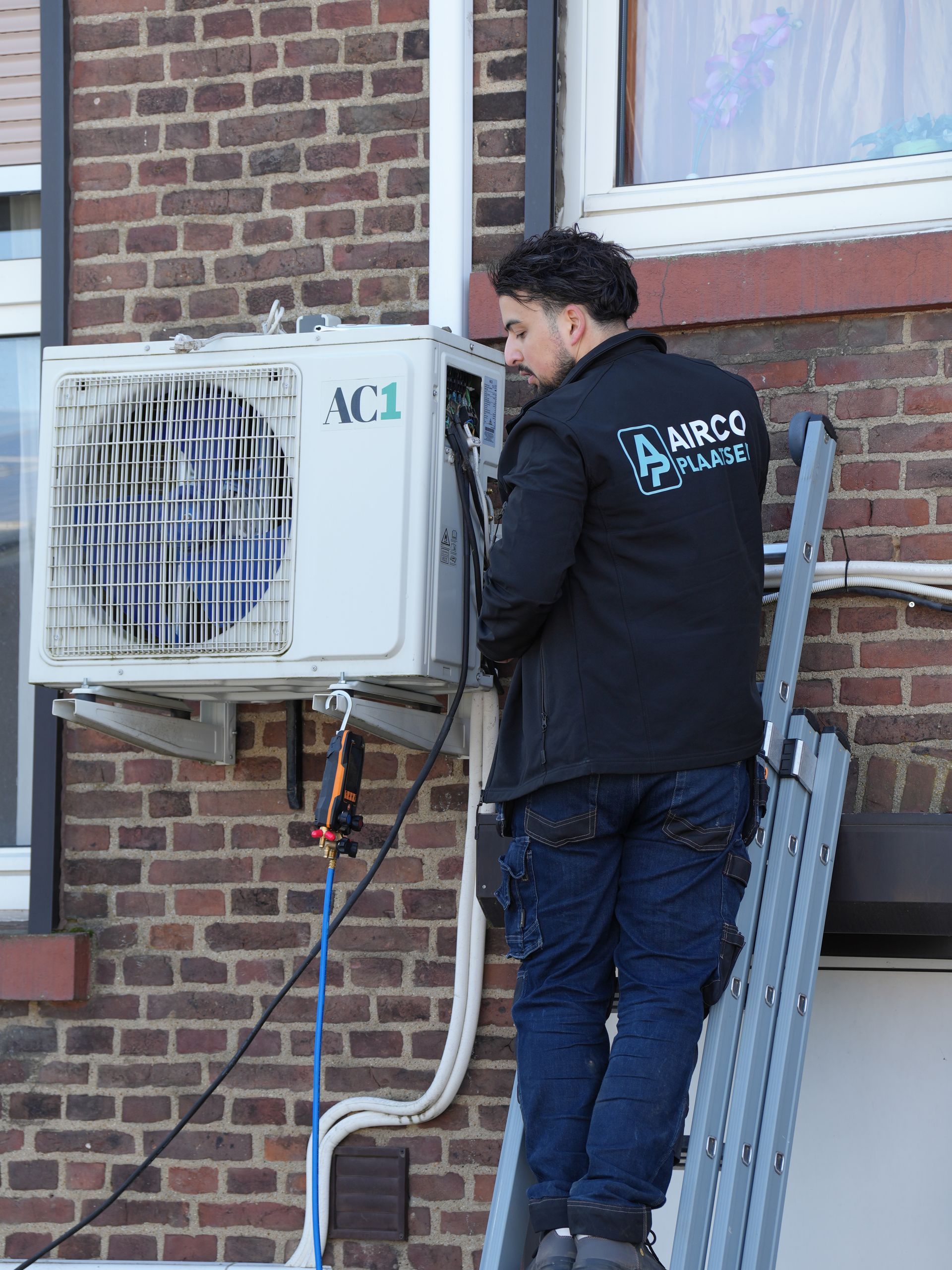 Een technicus inspecteert een aan de muur gemonteerde airconditioner buiten een bakstenen gebouw.