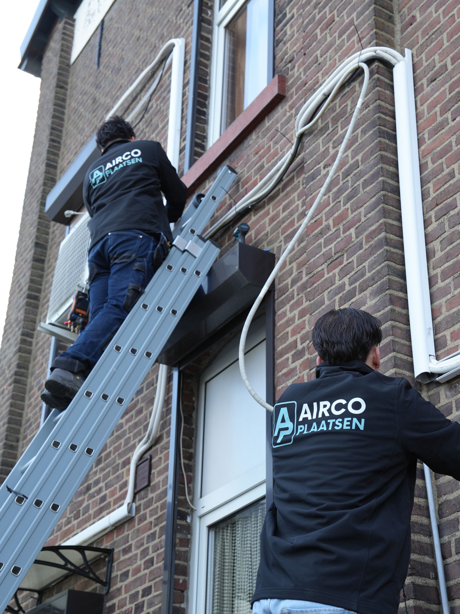 Twee arbeiders in zwarte shirts gebruiken een ladder om een ​​buitenmuur en