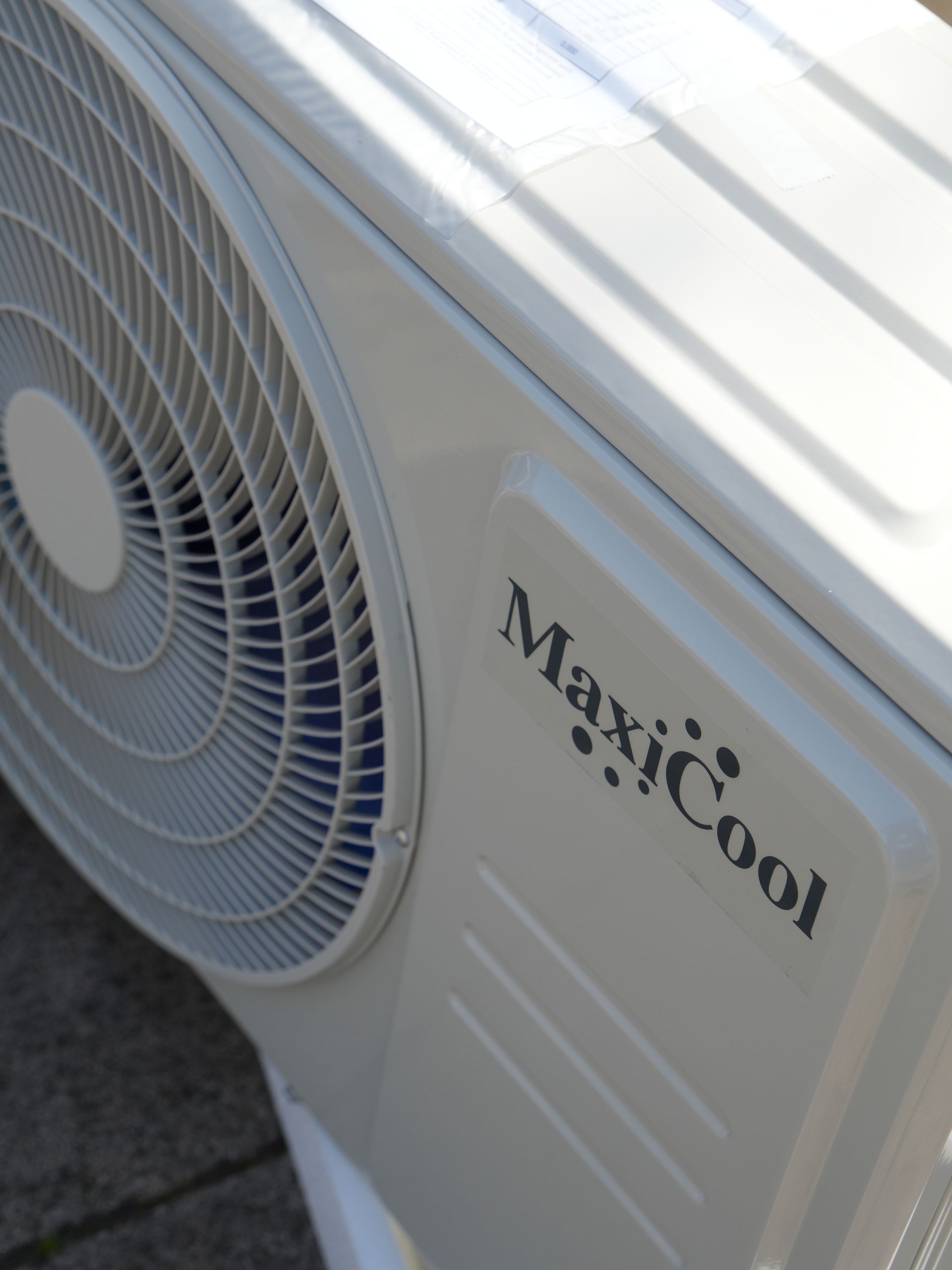 Detailopname van een witte MaxiCool airconditioner buitenunit met een groot ventilatorrooster.