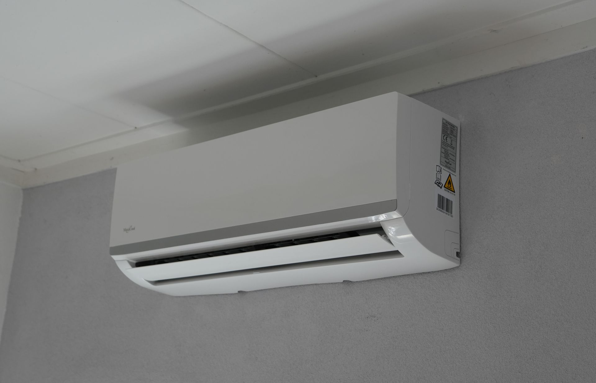 Witte, aan de muur gemonteerde airconditioner vlakbij het plafond in een grijze kamer.