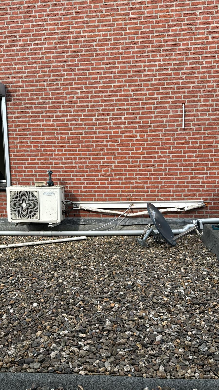 Een bakstenen muur met een airconditioningunit en een grijze duif die op het grind staat.
