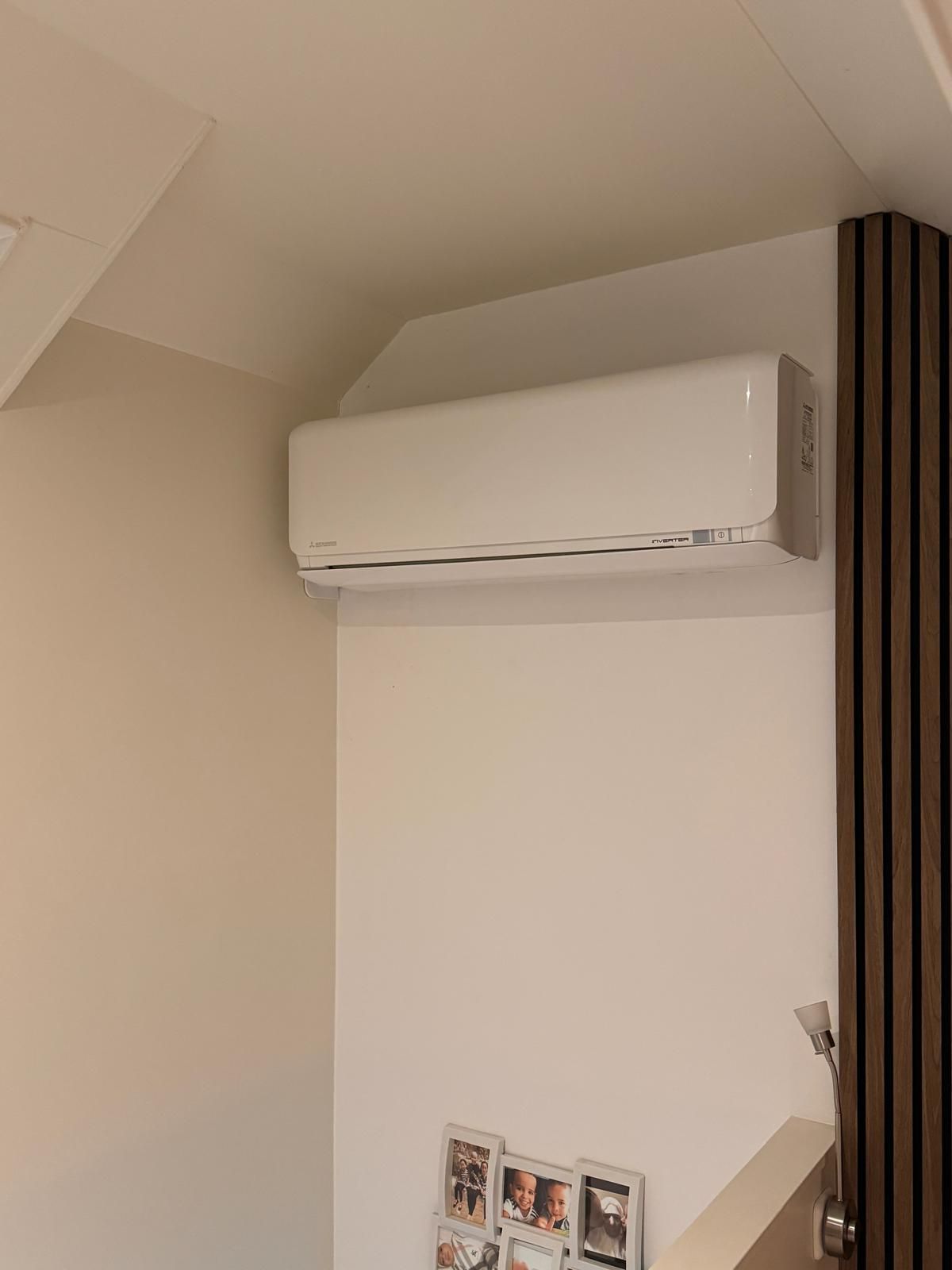 Witte, aan de muur gemonteerde airconditioner boven een trap in een beige kamer.