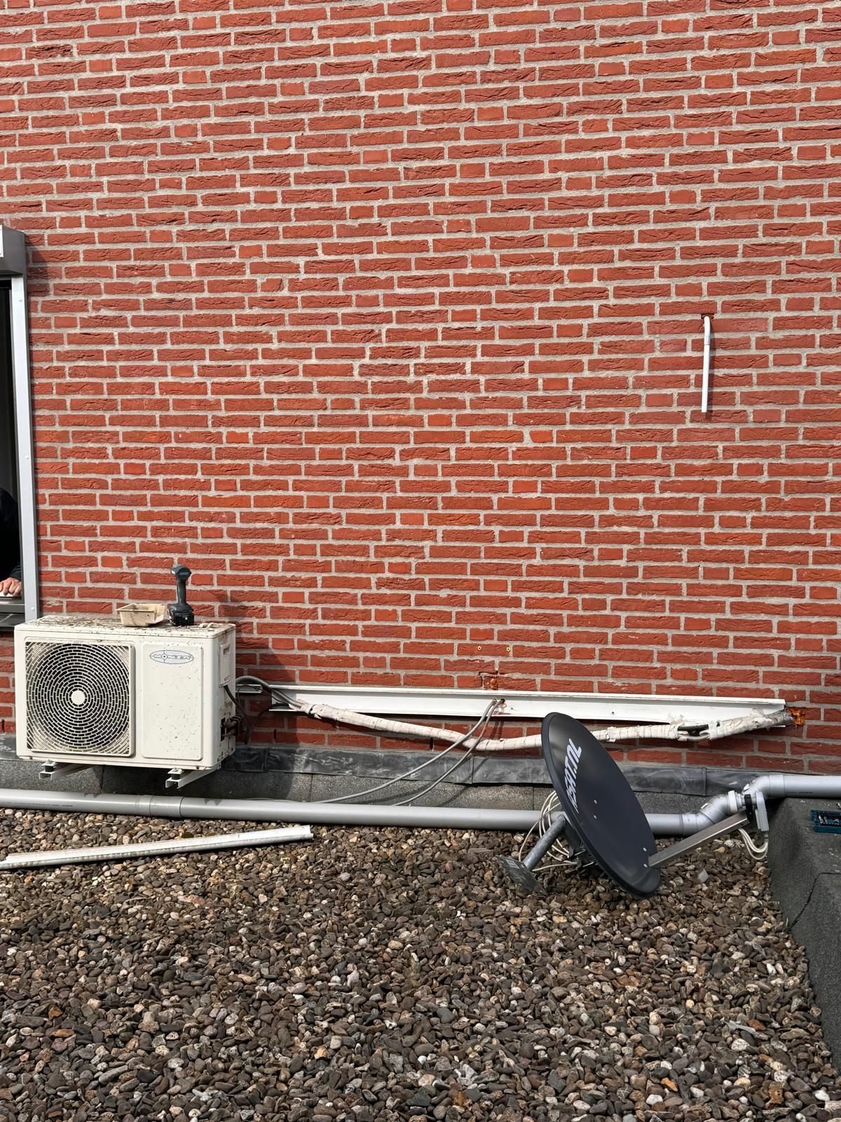Een bakstenen gebouwmuur met HVAC-units en dakapparatuur op een grindondergrond.
