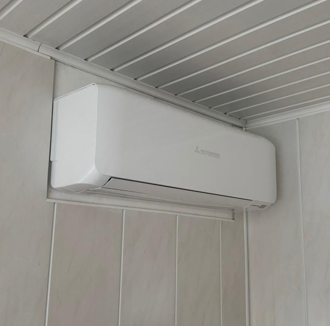 Witte wandairconditioner op een licht beklede wand onder een golfplaten plafond.