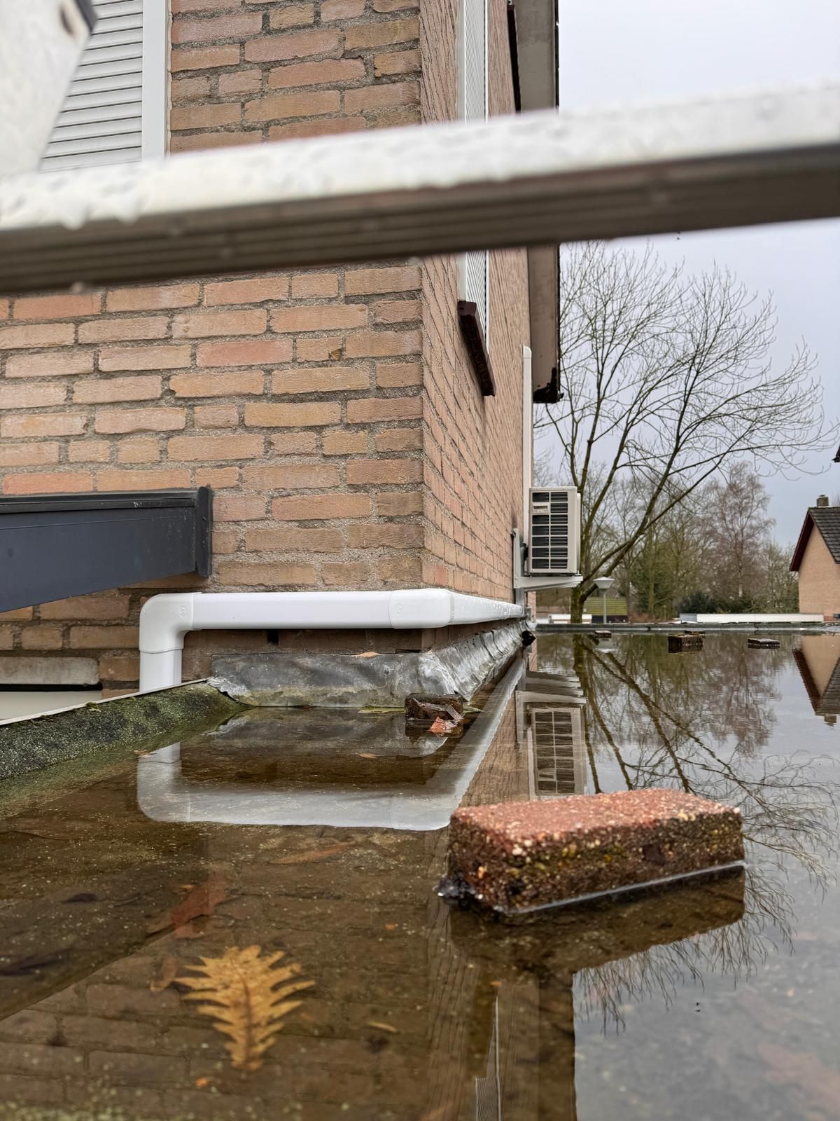 Overstromingswater omringt een bakstenen gebouw, met een blad dat in het water drijft en een baksteen die op een richel rust.