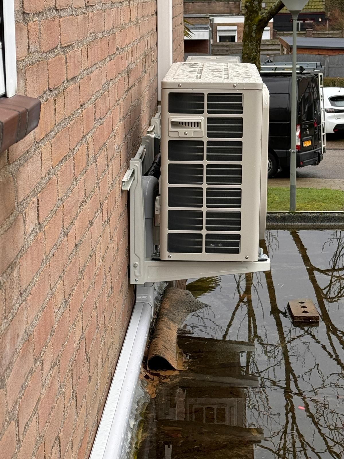Wandgemonteerde airconditioner op een bakstenen gebouw boven een natte steeg.