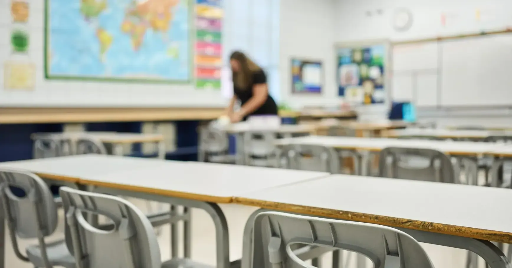 A woman is cleaning a classroom with tables and chairs.
