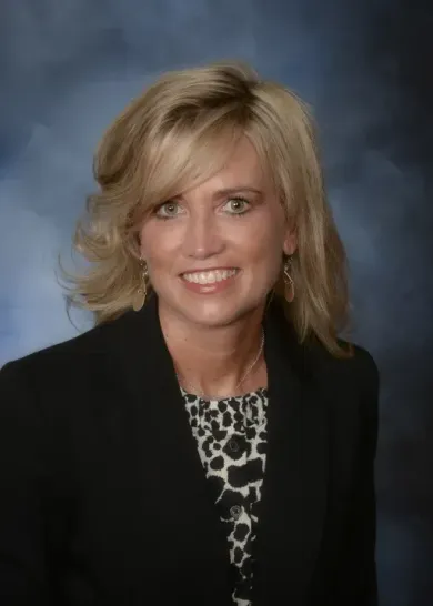 A woman in a black jacket and leopard print shirt smiles for the camera
