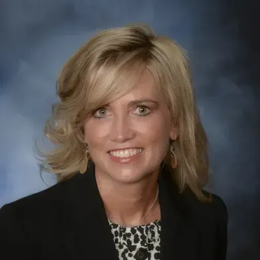 A woman in a black jacket and leopard print shirt smiles for the camera