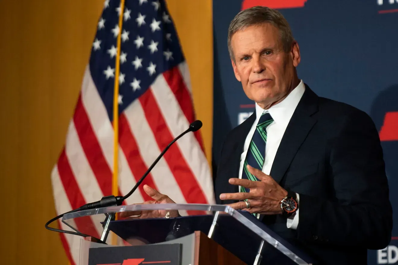 A man in a suit and tie is standing at a podium in front of an american flag.