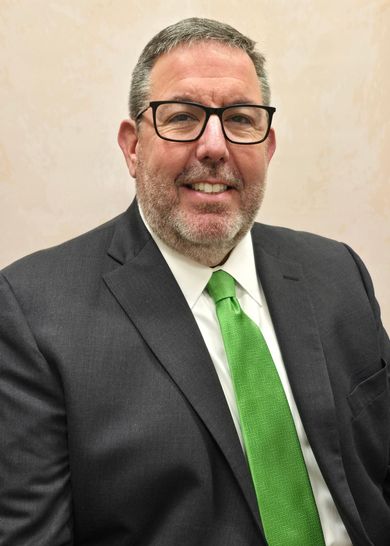 A man in a suit and tie is smiling in front of a wooden wall.