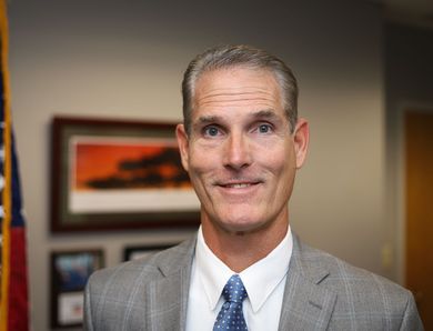 A man in a suit and tie is standing in front of an american flag.