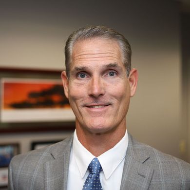A man in a suit and tie is standing in front of an american flag.