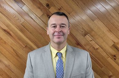 A man in a suit and tie is smiling in front of a wooden wall.
