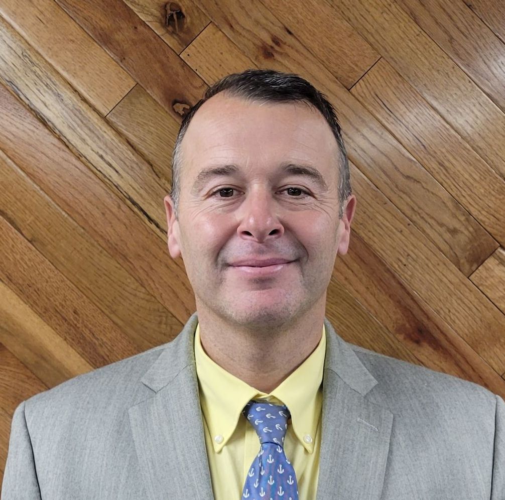 A man in a suit and tie is smiling in front of a wooden wall.