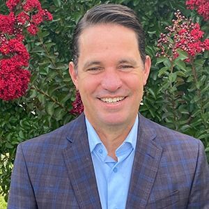A man in a suit and tie is smiling in front of a wooden wall.