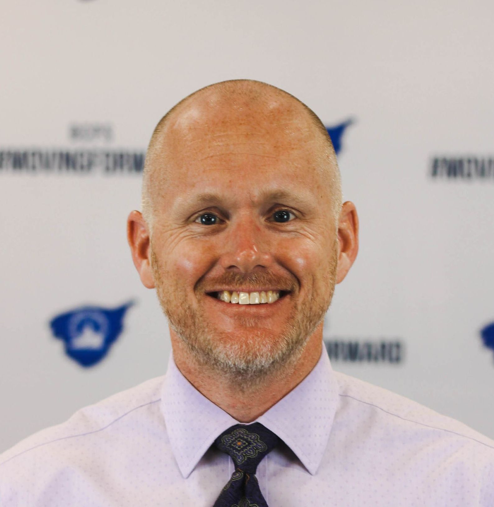 A bald man with a beard is smiling for the camera