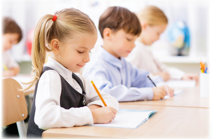 A group of children are sitting at desks in a classroom writing in notebooks.